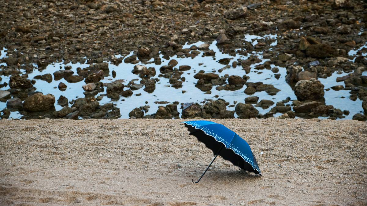 A large waterproof beach umbrella securely anchored on sandy shore with tilt mechanism extended over beach chairs
